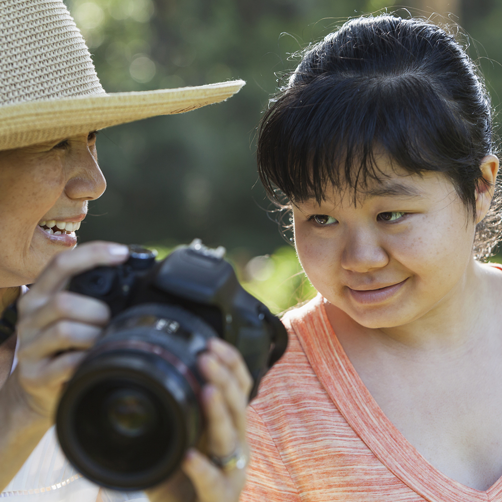 Mature Japanese woman (60s) showing photo on camera to autistic daughter (20s).