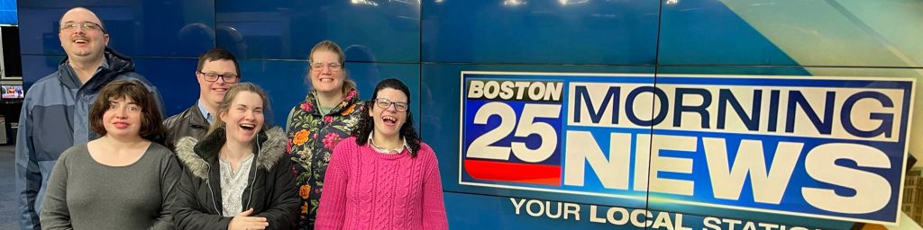 Smiling clients of the ARC in front of Boston 25 News screen