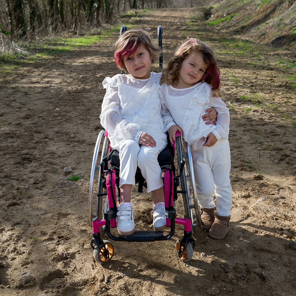 A girl in a wheelchair and her sister next to her
